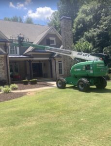 Screenshot | Wildlife Control Specialist of Atlanta Green telescopic boom lift extended to the roof of a stone house, worker standing on the platform.